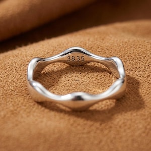 May include: A polished silver ring with a continuous wavy, undulating band design. The interior surface of the ring is clearly engraved with the number 3835, which is visible in the centre of the band. The metal has a smooth, reflective finish.