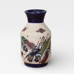 May include: A ceramic vase with a cream-colored body and a dark blue rim and base. The vase is decorated with a colorful bird and floral design in shades of brown, green, and blue. The vase is approximately 8 inches tall.