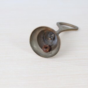 May include: A vintage brass bell with a handle, resting on a light-colored surface. The bell has a rounded shape with a small clapper inside. The handle is arched, and the bell appears aged.