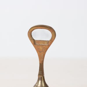 May include: A vintage brass bottle opener with a teardrop-shaped handle and a circular opening. The opener has a classic design and a polished finish, suggesting it is a barware item.