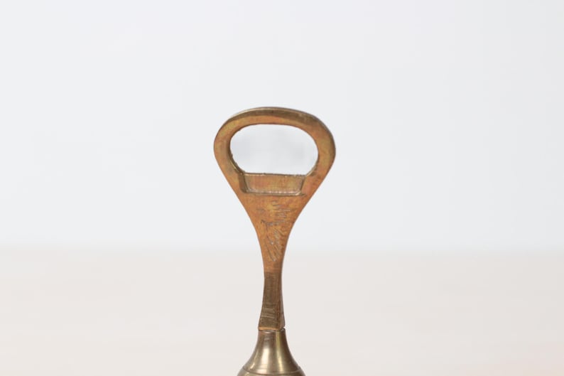 May include: A vintage brass bottle opener with a teardrop-shaped handle and a circular opening. The opener has a classic design and a polished finish, suggesting it is a barware item.