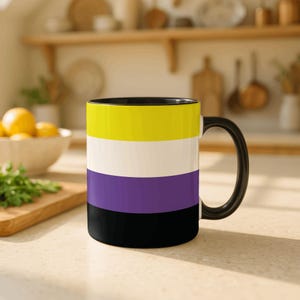 May include: A ceramic mug with a black handle and interior. The mug features a non-binary pride flag design with horizontal stripes in yellow, white, purple, and black. The mug is sitting on a light-colored surface.