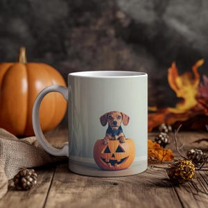 May include: A white ceramic mug featuring a brown and black dachshund puppy inside a carved orange pumpkin. The pumpkin has a jack-o'-lantern face. The mug is on a wooden surface with a pumpkin and fall foliage in the background.
