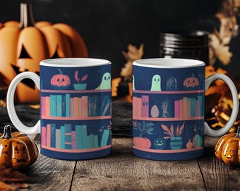 Può includere: Due tazze in ceramica bianca con un design blu scuro raffigurante una libreria con libri, zucche, fantasmi e piante. Le tazze sono su una superficie di legno con zucche e foglie.
