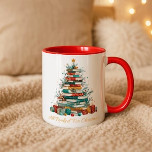 May include: White ceramic mug with a red interior and handle. The mug features a Christmas tree design made of stacked books, with the text "All Booked For Christmas" at the bottom. The design includes a gold star and gift boxes.