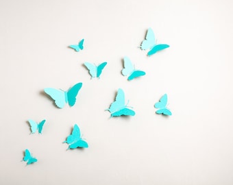 May include: A white wall with multiple blue and turquoise paper butterflies of various sizes and shapes.