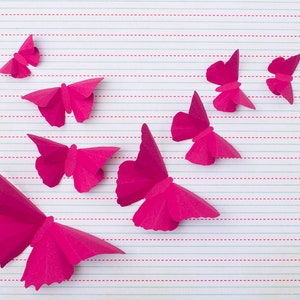May include: A collection of pink paper butterflies arranged on a lined sheet of paper. The butterflies are all different sizes and shapes, and they are all facing different directions.