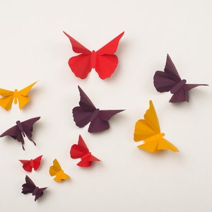 May include: A collection of paper butterflies in various colors, including red, orange, yellow, and purple. The butterflies are arranged on a white background.