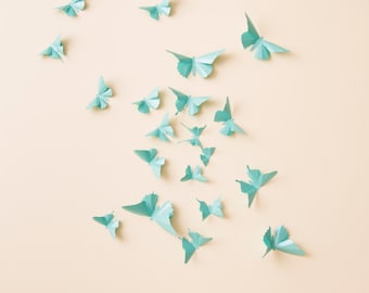 May include: A light beige wall decorated with numerous teal paper butterflies of various sizes. The butterflies are arranged in a random pattern, creating a whimsical and airy aesthetic.