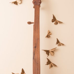 May include: A wooden banjo with a light brown finish and gold accents. The banjo is surrounded by paper butterflies in various shades of brown.