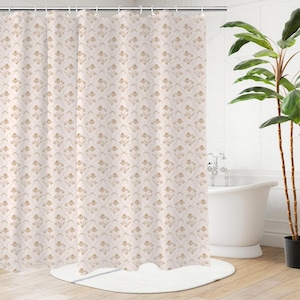 Op de afbeelding: Beige douchegordijn met een herhalend bloemmotief in goud- en crèmetinten. Het gordijn hangt voor een witte badkuip en een plant in pot.