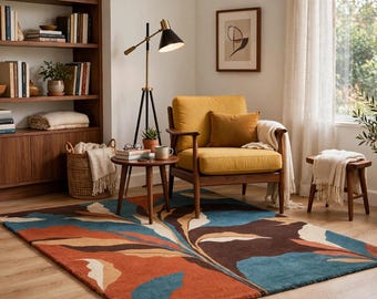 May include: A rectangular area rug featuring a large-scale abstract botanical pattern in shades of deep blue, burnt orange, dark brown, and cream. The rug is positioned on a light wood floor in a room with a yellow armchair, a wooden side table, and a lamp.