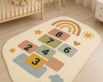 May include: A cream-colored hopscotch rug with colorful squares numbered 2 through 8, plus a 3. The rug features a rainbow, sun, stars, and clouds. The rug is designed for a child's room.
