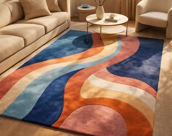 Op de afbeelding: Een rechthoekig vloerkleed met een retro-ontwerp. Het vloerkleed heeft een golvend patroon in tinten blauw, oranje, roze en crème. Het vloerkleed ligt op een houten vloer in een woonkamer.