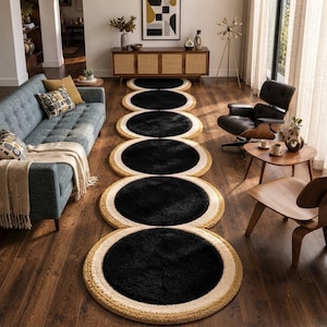 May include: A long runner rug featuring a series of connected circular segments. Each circle has a solid black center, a white middle ring, and a textured mustard yellow outer border. The rug is laid out on a dark wood floor in a living room.