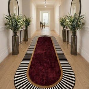 Puede incluir: Una alfombra de pasillo larga y ovalada con un centro de color burdeos intenso, un borde dorado fino y un borde exterior ancho con rayas radiales blancas y negras. La alfombra está situada en un pasillo entre dos jarrones de vidrio texturizado.