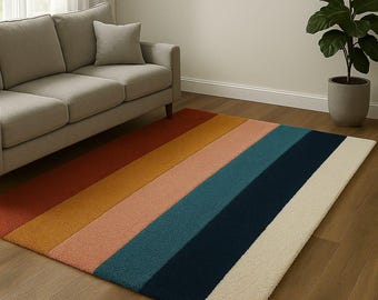 May include: A rectangular area rug with a striped design in shades of red, orange, yellow, pink, teal, navy, and cream. The rug is placed on a hardwood floor in front of a gray sofa. The text "SANAHEB RUGS" is visible.