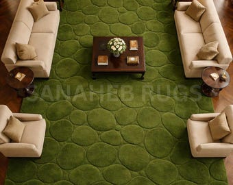 May include: Overhead view of a living room with a large, olive green rug featuring a pebble design. Beige sofas and armchairs surround a dark wood coffee table with flowers. The room has hardwood floors and a fireplace.