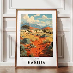 Könnte beinhalten: Gerahmter Kunstdruck einer namibischen Landschaft. Das Kunstwerk zeigt einen rot-orangen Pfad, der zu Bergen unter einem blauen Himmel mit Wolken führt. Der Druck trägt die Aufschrift "Afrika Namibia". Der Rahmen ist braun.