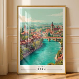 May include: A framed art print of Bern, Switzerland, featuring a vibrant cityscape with red-roofed buildings, a turquoise river, and a bridge. The artwork is set against a backdrop of mountains and a clear sky. The print is in a gold frame.