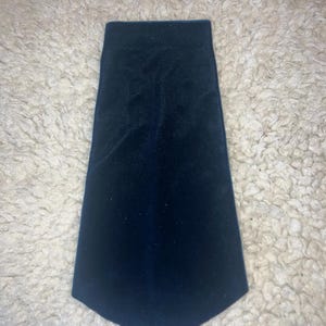 Może przedstawiać: Ciemnoniebieski aksamitny krawat o lekko zwężającym się kształcie. Krawat wykonany jest z miękkiego, pluszowego materiału i ma gładką fakturę. Krawat to klasyczny dodatek do formalnego stroju.