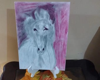Op de afbeelding: Potloodtekening van een paardenhoofd, weergegeven in grijstinten en wit, tegen een roze en paarse achtergrond. Het kunstwerk wordt getoond op een witte ezel, met herfstbladeren aan de basis.