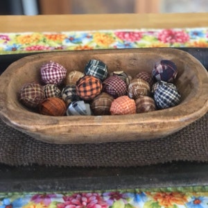 Pu&ograve; includere: Una ciotola in legno poco profonda di forma ovale riempita con una collezione di piccole sfere rivestite in tessuto. Le sfere presentano vari motivi a quadri e scozzesi in colori tra cui arancione, marrone, blu, verde e bianco.