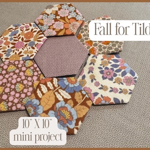 May include: A collection of seven fabric hexagons arranged in a flower pattern, featuring various floral prints in shades of brown, pink, blue, and cream. The text Fall for Tilda and 10 X 10 mini project is visible on the image.