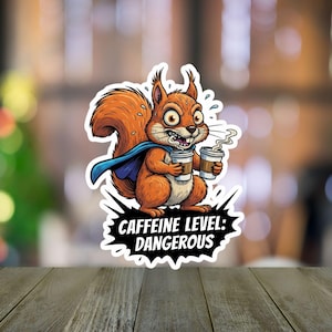 May include: A sticker featuring a cartoon squirrel with wide eyes, holding two coffee cups. The squirrel wears a blue cape and appears stressed. The text "CAFFEINE LEVEL: DANGEROUS" is in a black speech bubble.