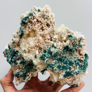 Könnte beinhalten: Eine natürliche Mineralprobe mit einer Kombination aus Farben und Texturen. Das Stück zeigt eine Mischung aus cremeweißen, beigen und tiefen tealgrünen Farbtönen. Das Mineral hat eine kristalline Struktur mit einer rauen, unebenen Oberfläche.