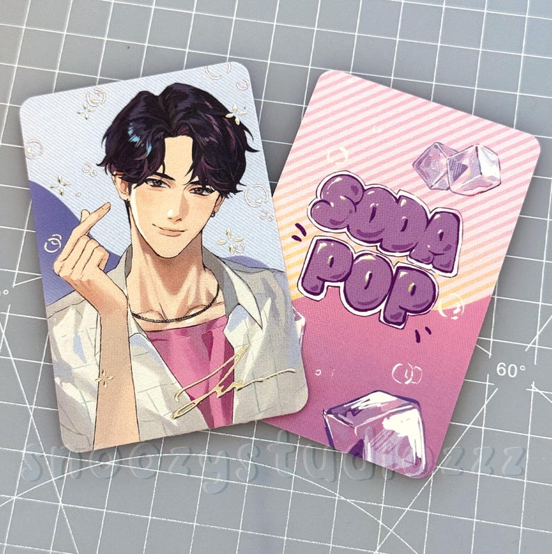 K&ouml;nnte beinhalten: Zwei rechteckige Sammelkarten mit abgerundeten Ecken. Eine Karte zeigt eine Anime-Illustration einer Person mit dunklem Haar, die ein Fingerherz formt. Die andere Karte zeigt den Text SODA POP in Lila mit Grafiken von Eisw&uuml;rfeln.