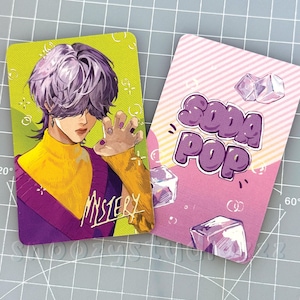 K&ouml;nnte beinhalten: Zwei rechteckige Sammelkarten. Die linke Karte zeigt eine Anime-Figur mit violettem Haar, gelbem Rollkragenpullover und violetter Weste, mit dem Wort MYSTERY in Gelb. Die rechte Karte ist rosa mit dem Text SODA POP und Eisw&uuml;rfeln.