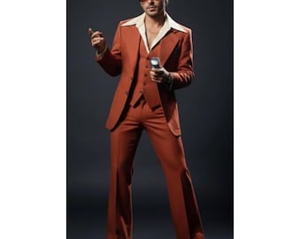 May include: A rust-colored three-piece suit with wide-leg pants, a collared shirt, and sunglasses. The suit includes a blazer, vest, and trousers. The outfit has a retro style, reminiscent of the 1970s. The letters "ZB" are in the top right corner.