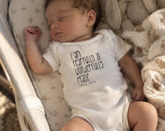 Puede incluir: Un body de bebé de manga corta en color blanco con el texto impreso en negro I am fearfully & wonderfully made Psalm 139:14. La prenda está diseñada para bebés e incluye un cierre de botones a presión en la parte inferior.