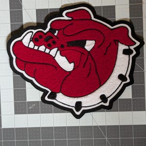 May include: A red and white bulldog patch with a black border. The patch is approximately 9 inches in size. The bulldog's face is red with white accents and a white background. The text "Red/White Bulldog 9" is at the top.
