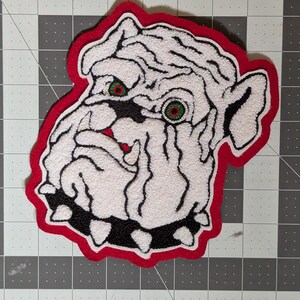 May include: White Bulldog 6" patch with a red border. The patch features a white bulldog head with black and red accents. The bulldog has green eyes and a black studded collar. The patch is approximately 6 inches in size.