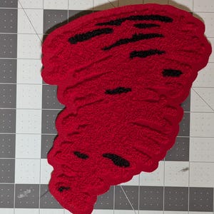 May include: A red tornado-shaped patch, approximately 6 inches in height, with black horizontal accents. The text "Red Tornado 6" is displayed at the top. The patch is on a gray and white grid.