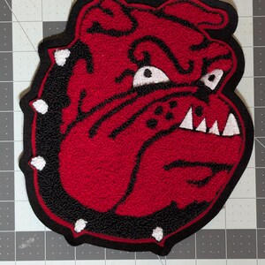 May include: A red and black bulldog patch, approximately 7 inches in size. The patch features a detailed design of a bulldog's face with white teeth and eyes. The text "Red/Black Bulldog 7" is displayed at the top.