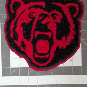 May include: A red and black bear patch, approximately 8 inches in size, with a detailed design of a roaring bear's face. The bear's face is red, outlined in black, and the text "Red/Black Bear 8"" is at the top.