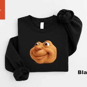 May include: Black crewneck sweatshirt featuring a cartoonish, smiling face in shades of brown and tan. The word "Black" is printed in white on the lower right. The brand "Pixulo." is in the upper left corner.
