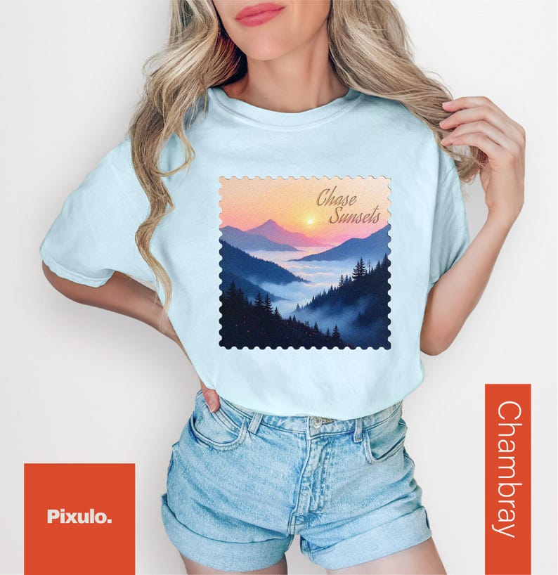 May include: Light blue t-shirt with a landscape graphic featuring mountains, a sunset, and the text "Chase Sunsets." The shirt is paired with denim shorts. The graphic is framed with a decorative border.