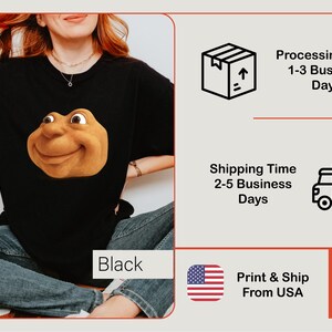 May include: Black t-shirt featuring a smiling, cartoonish face in shades of brown and tan. The word "Black" is visible in a white box. The image also includes shipping and processing information.