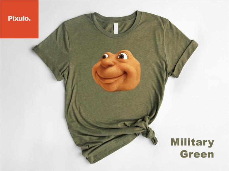 May include: Olive green t-shirt featuring a smiling, cartoonish face in shades of brown and tan. The shirt has short sleeves and a crew neck. The words "Military Green" are printed on the bottom right.