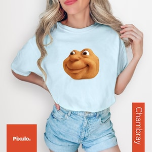 May include: Light blue t-shirt featuring a cartoon character with a smiling face. The shirt is paired with denim shorts. The word "Chambray" is printed vertically on the right side of the image. The Pixulo logo is in the bottom left corner.