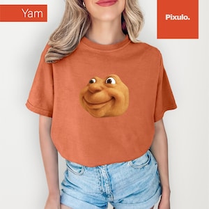 May include: Orange t-shirt with a smiling, cartoonish face graphic. The word "Yam" is in a box in the upper left corner. The shirt is paired with denim shorts.
