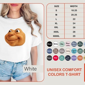 May include: White unisex comfort colors t-shirt featuring a smiling, cartoonish face. The shirt has a size chart and color options. The text "Pixulo" is in the bottom right corner.