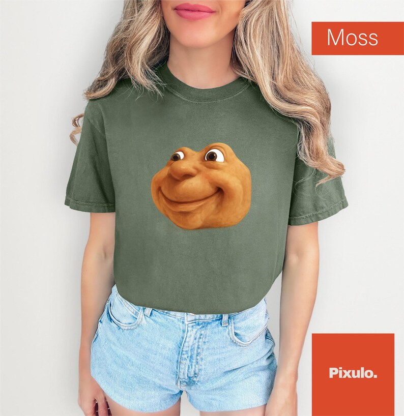 May include: A moss green t-shirt featuring a cartoonish, smiling face. The graphic is a warm, golden brown color. The shirt is paired with blue denim shorts. The word "Moss" is in a red box in the upper right corner.