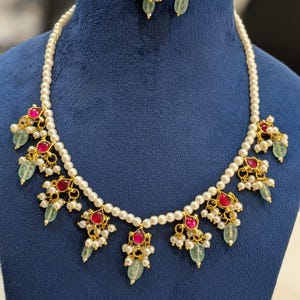 May include: A gold-toned necklace and earring set with a pearl strand and ornate pendants. The pendants feature red gemstones, small white pearls, and green teardrop-shaped stones. The text "FW75" is in the upper right corner.