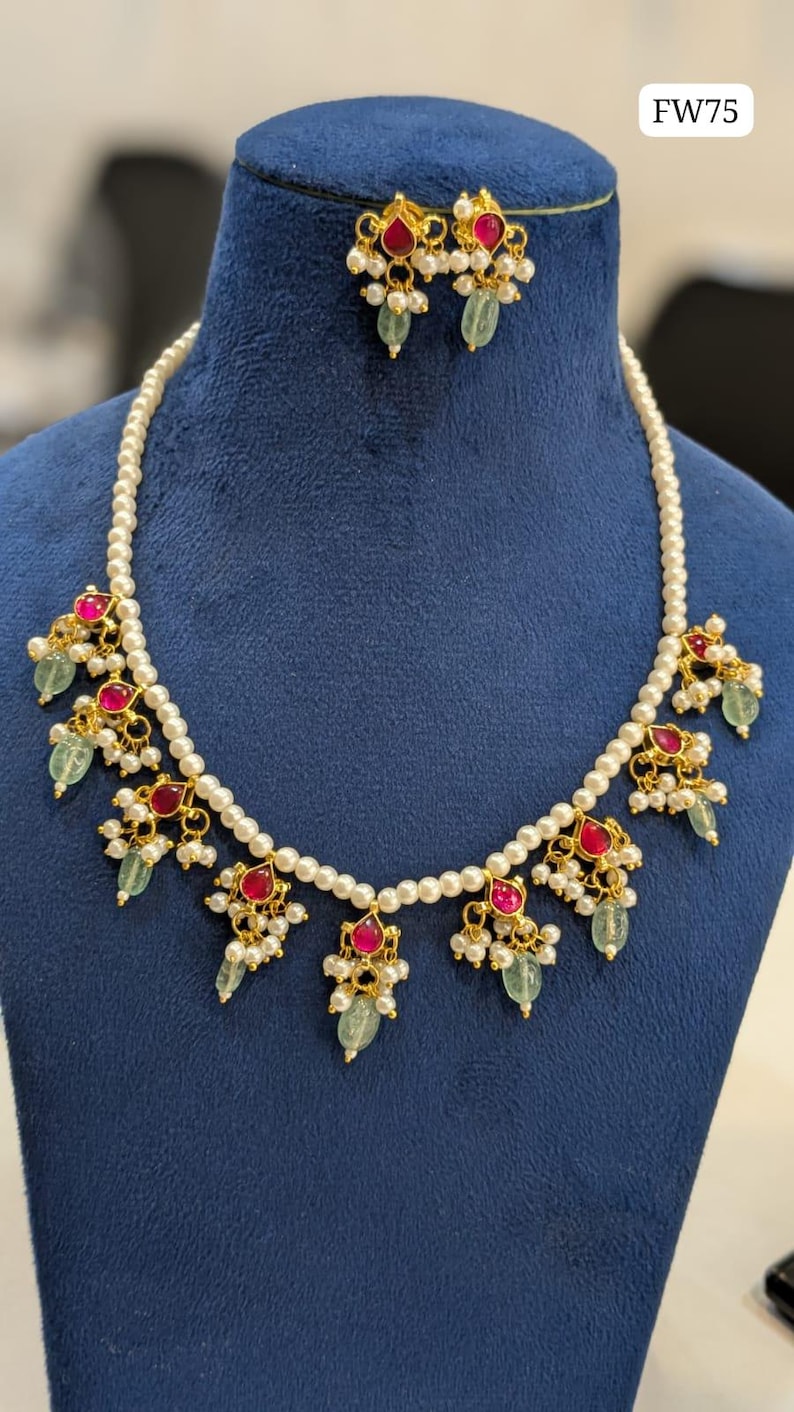 May include: A gold-toned necklace and earring set with a pearl strand and ornate pendants. The pendants feature red gemstones, small white pearls, and green teardrop-shaped stones. The text "FW75" is in the upper right corner.