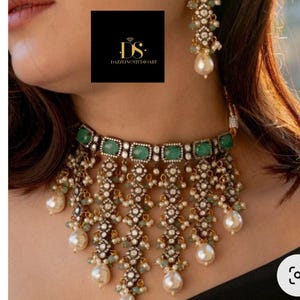 May include: An ornate necklace and earring set featuring emerald-colored stones and dangling pearl accents. The jewelry has a gold-colored metal setting with intricate detailing. The image also includes the text "DAZZLINGSTUDIOART".